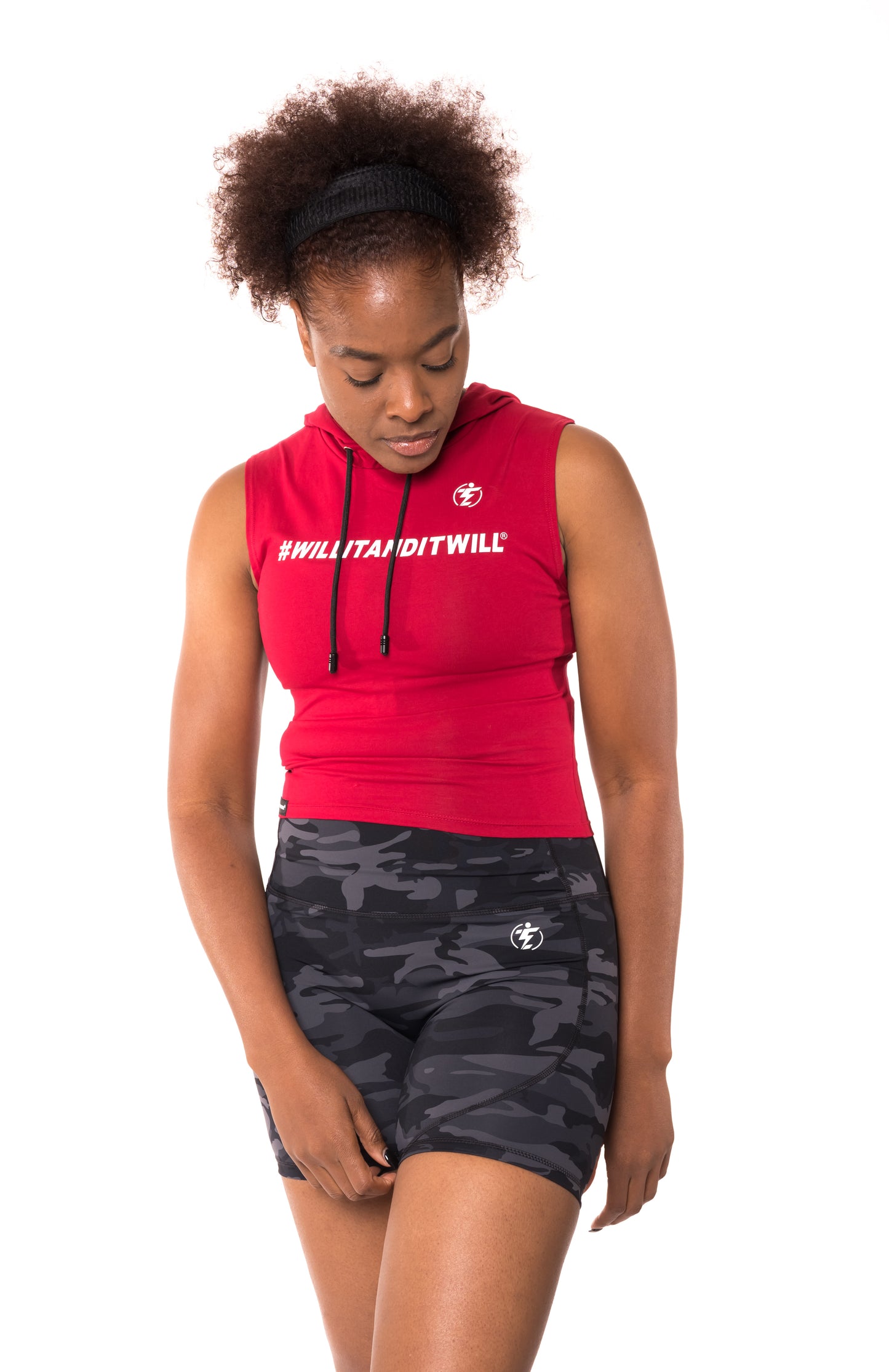 Woman in red sleeveless hoodie with '#WILLITANDITWILL' and camo print bike shorts.