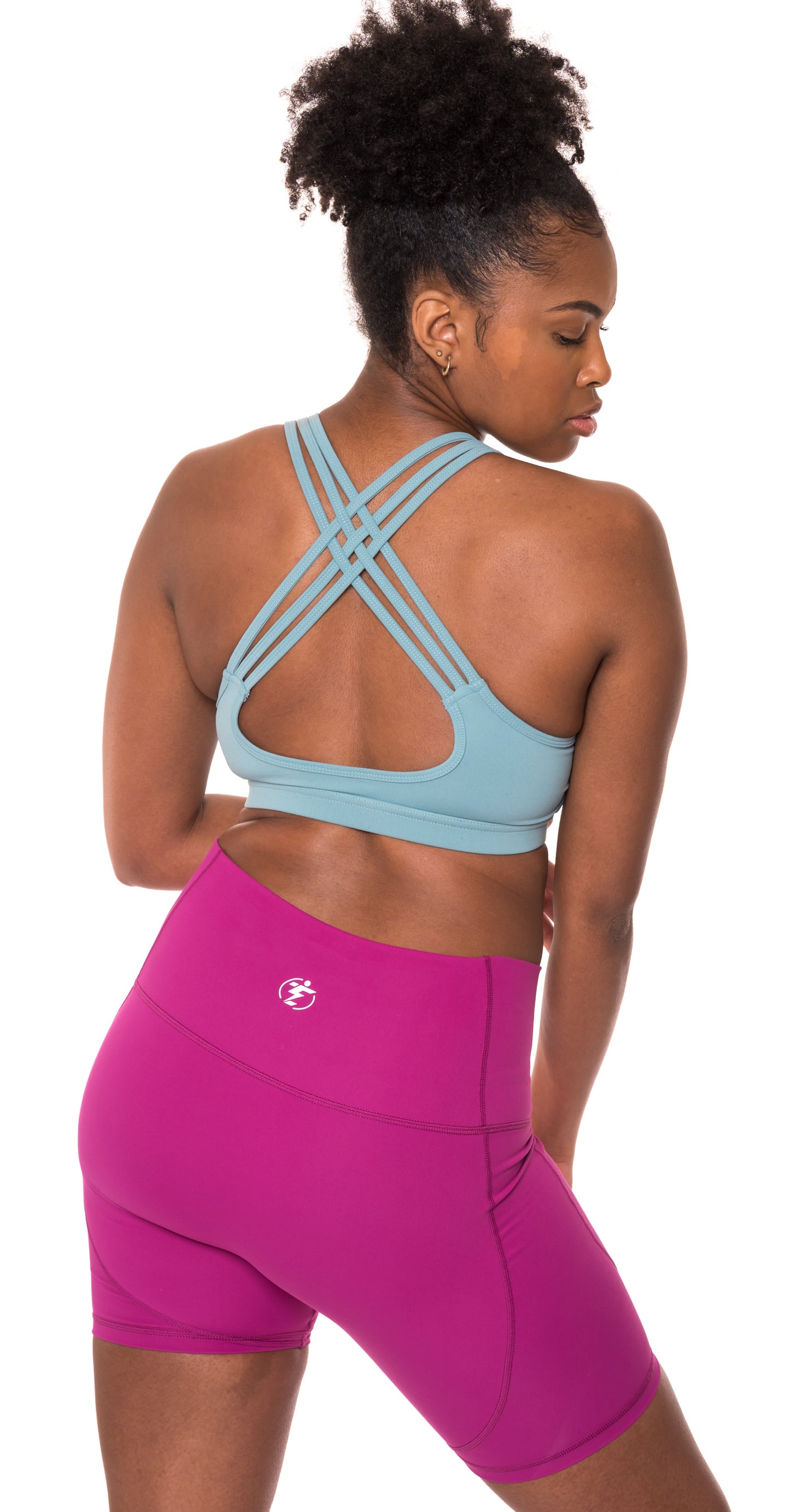 Woman wearing a blue strappy sports bra and magenta biker shorts, back view.