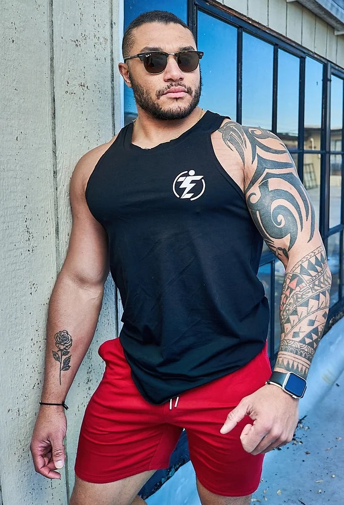 Man wearing a black tank top with logo and red athletic shorts.