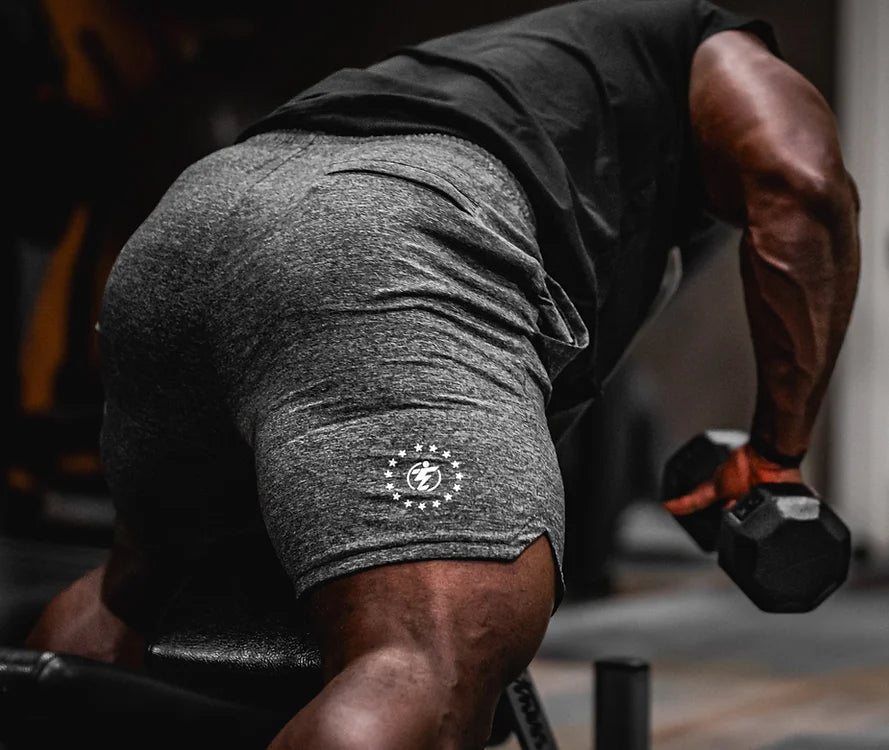 Man lifting dumbbell wearing gray athletic shorts with logo.