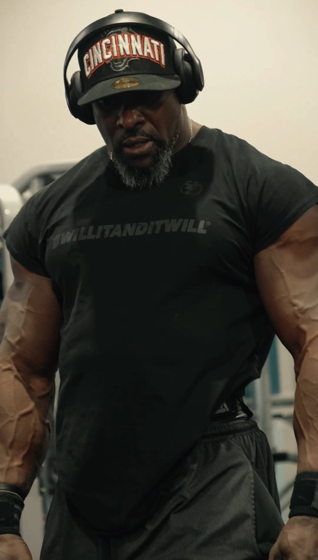 Person wearing a black t-shirt with text and a helmet with 'Cincinnati' on it, standing in a gym.