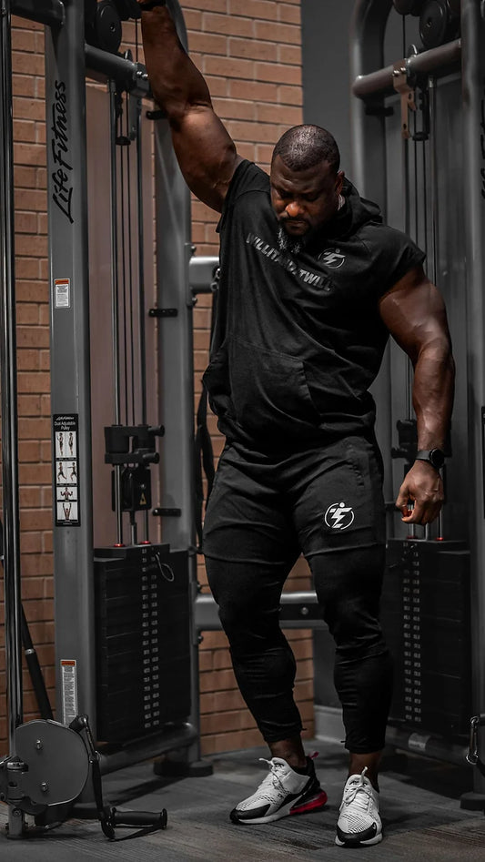 Man using Life Fitness cable machine in black hoodie, shorts and Nike sneakers. Gym workout.