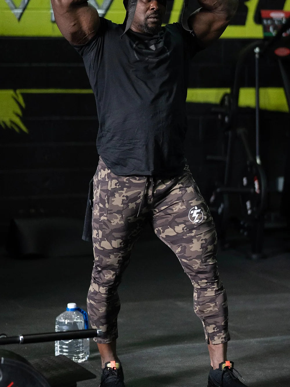 Man lifting weights in camo joggers. Camouflage athletic pants with logo detail.