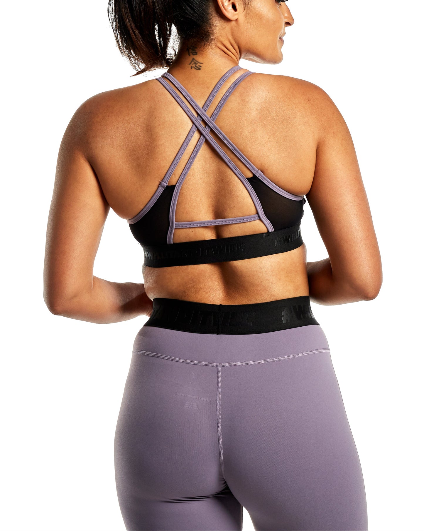 Woman wearing a black sports bra with lilac straps and matching leggings, back view.