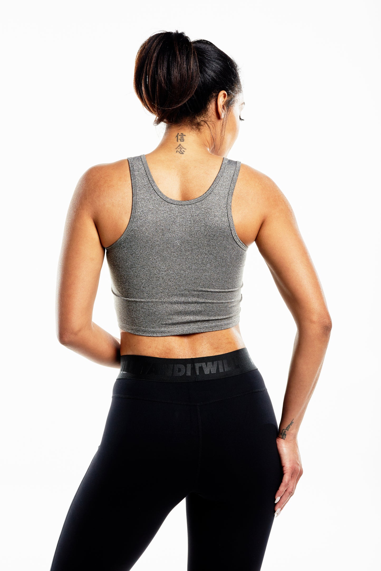 Back view of a woman wearing a gray crop top and black leggings, showcasing activewear.
