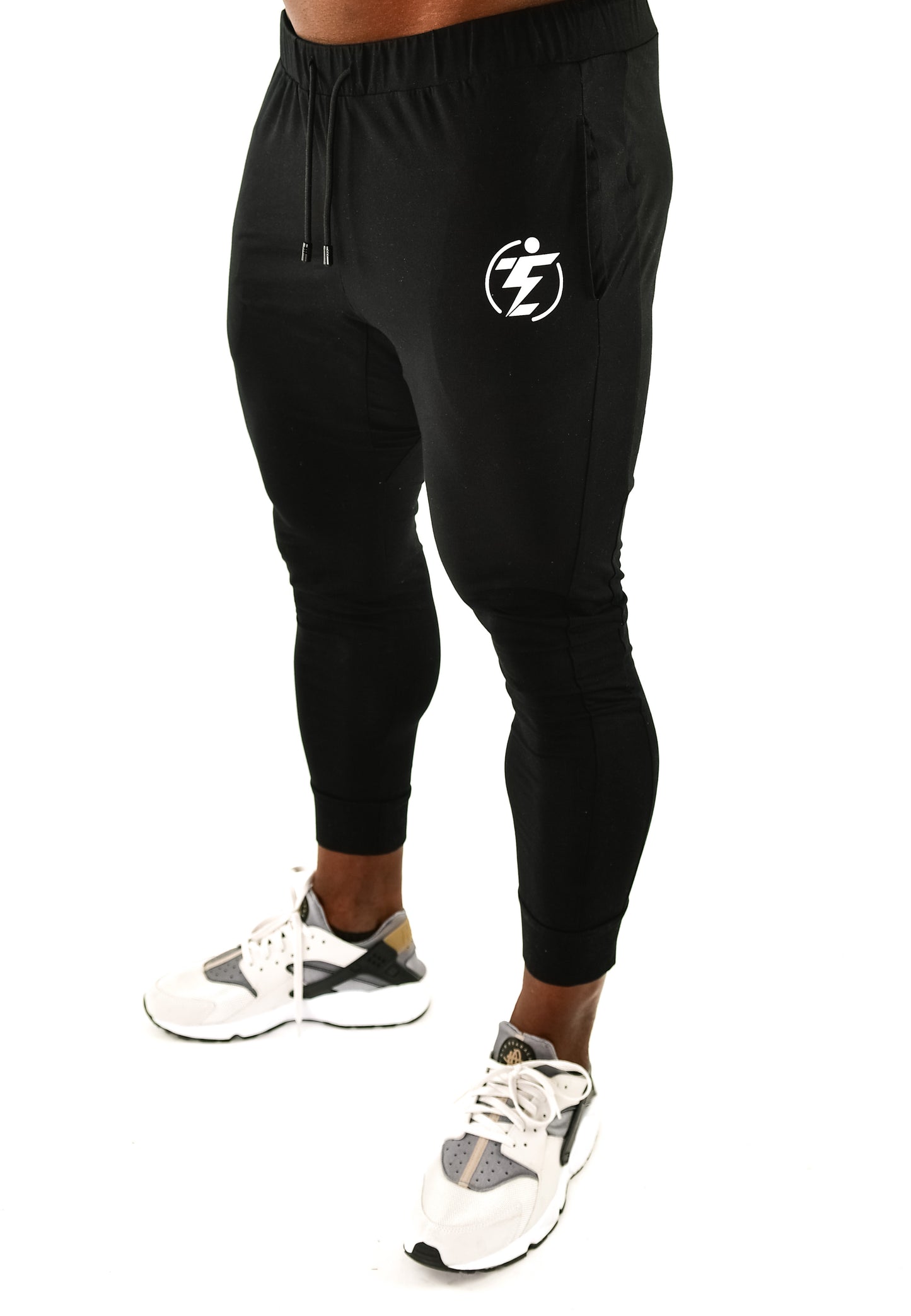 Model wearing black drawstring joggers with white logo and white and gray sneakers.