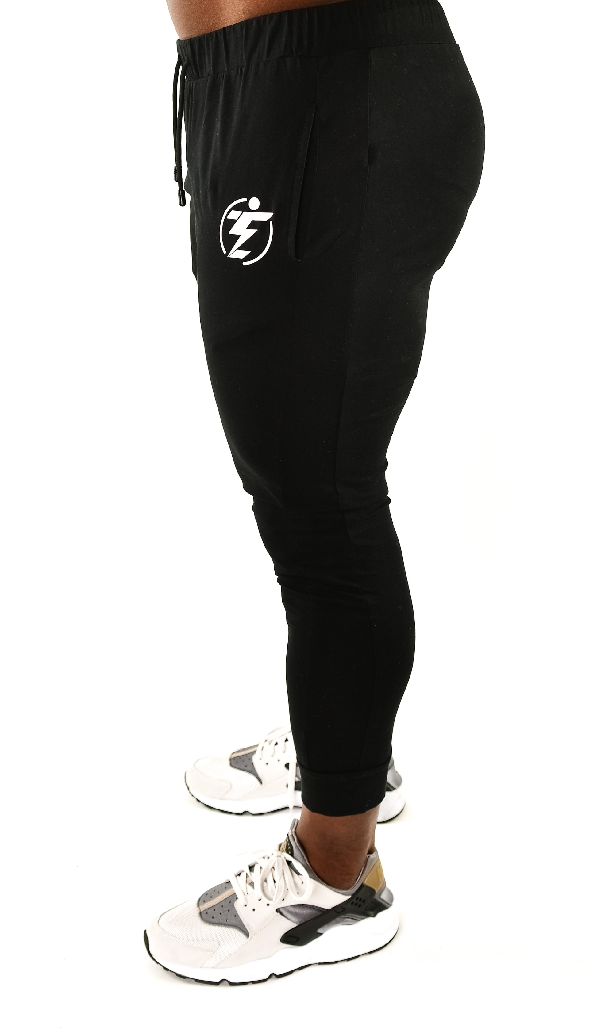 Side view of black slim-fit joggers with logo and drawstring, paired with white running shoes.