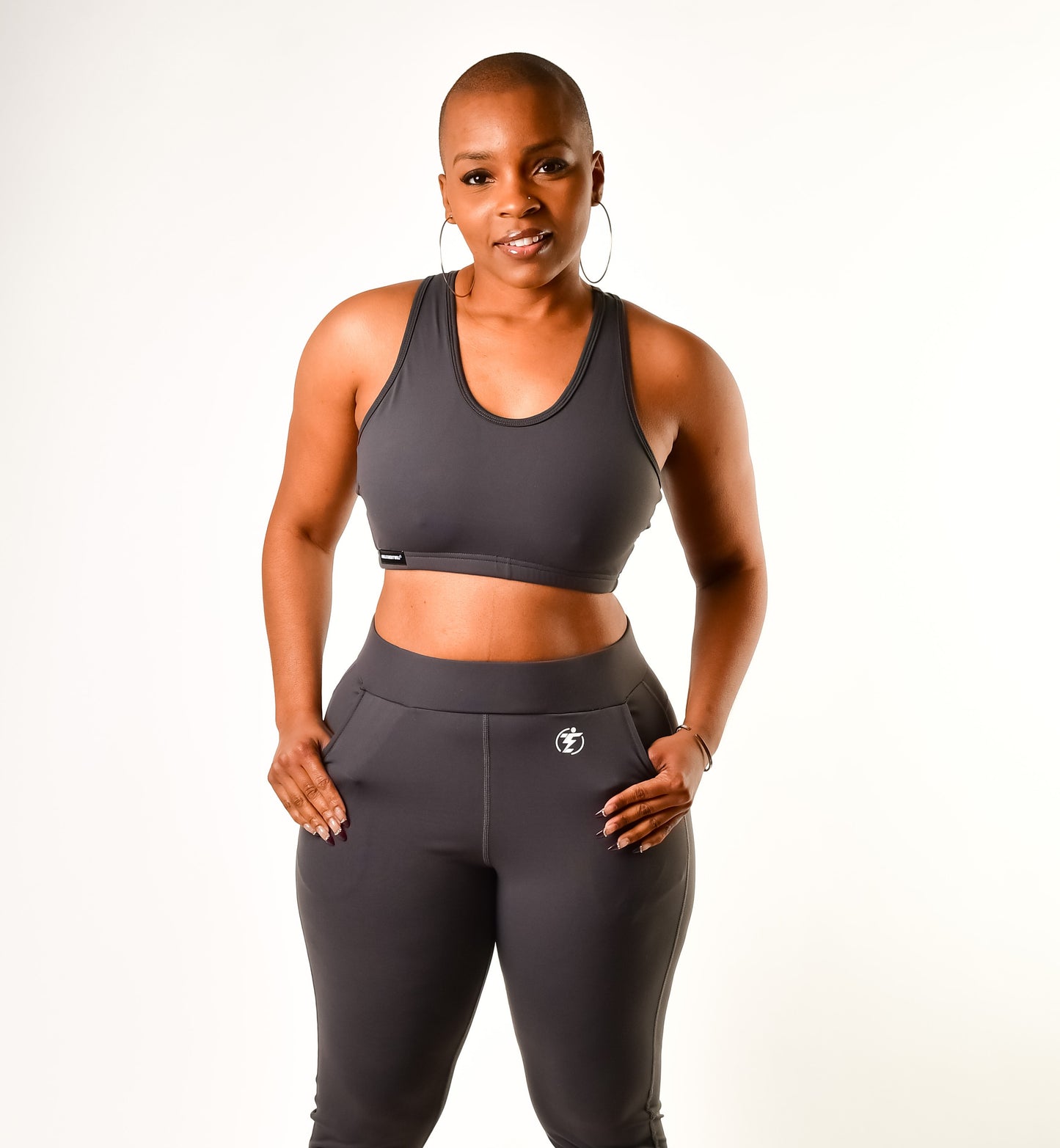 Woman in gray athletic wear, sports bra and joggers with pockets, hands in pockets.
