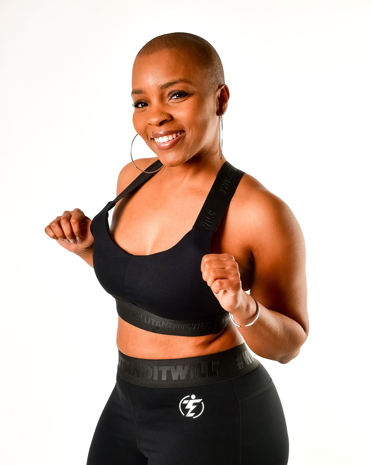 Woman in black sports bra and leggings with logo, smiling confidently.