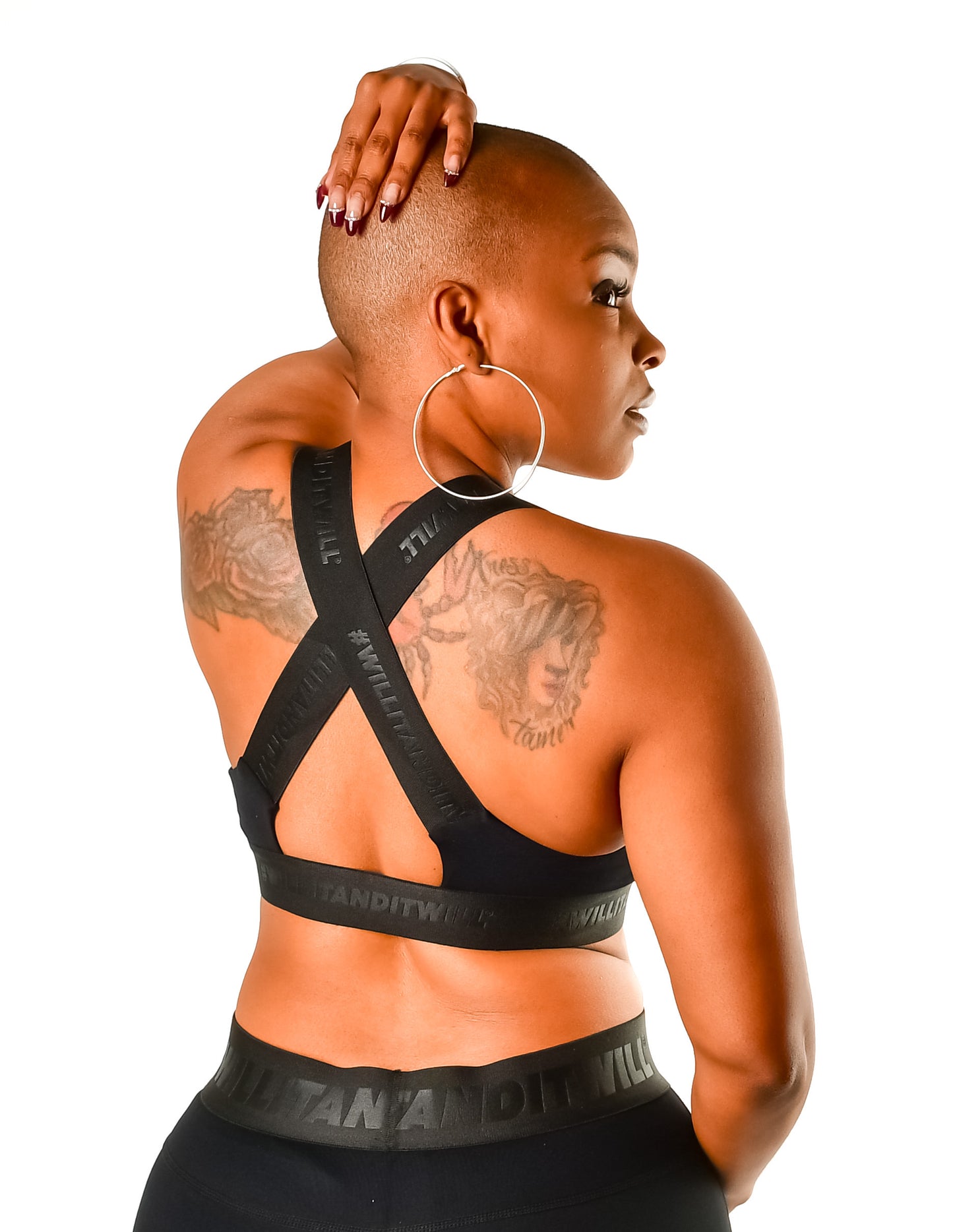 Woman in black sports bra and leggings, back view. Cross-back straps and waistband feature 'Will It Stand It Will' logo.