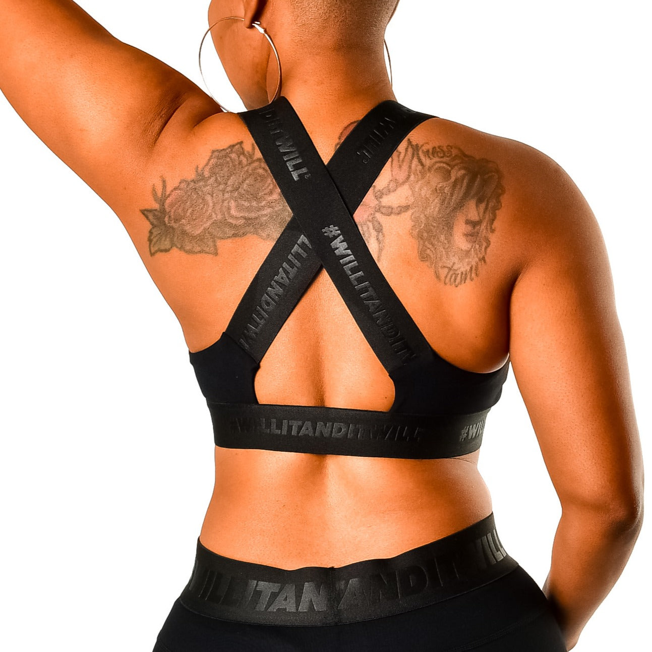 Black sports bra with criss-cross straps featuring '#WILLITANDITWILL' on the band, worn by a woman with tattoos.