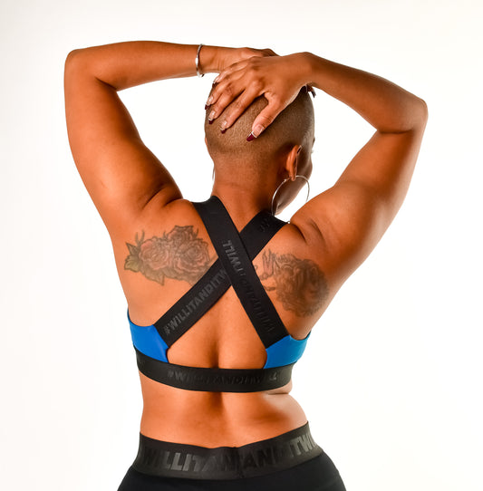 Woman wearing a blue and black sports bra with criss-cross straps, showcasing the brand name. Back view.
