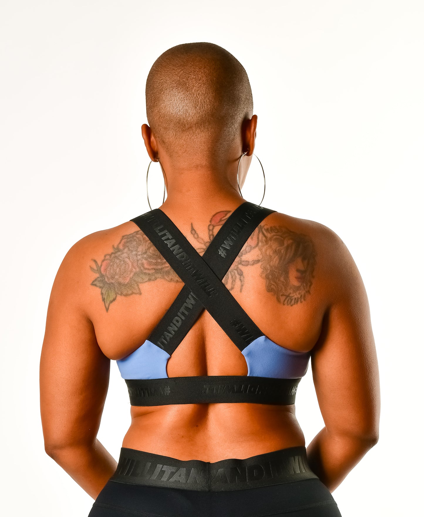 Back view of woman in blue sports bra with black branded straps and matching black leggings.