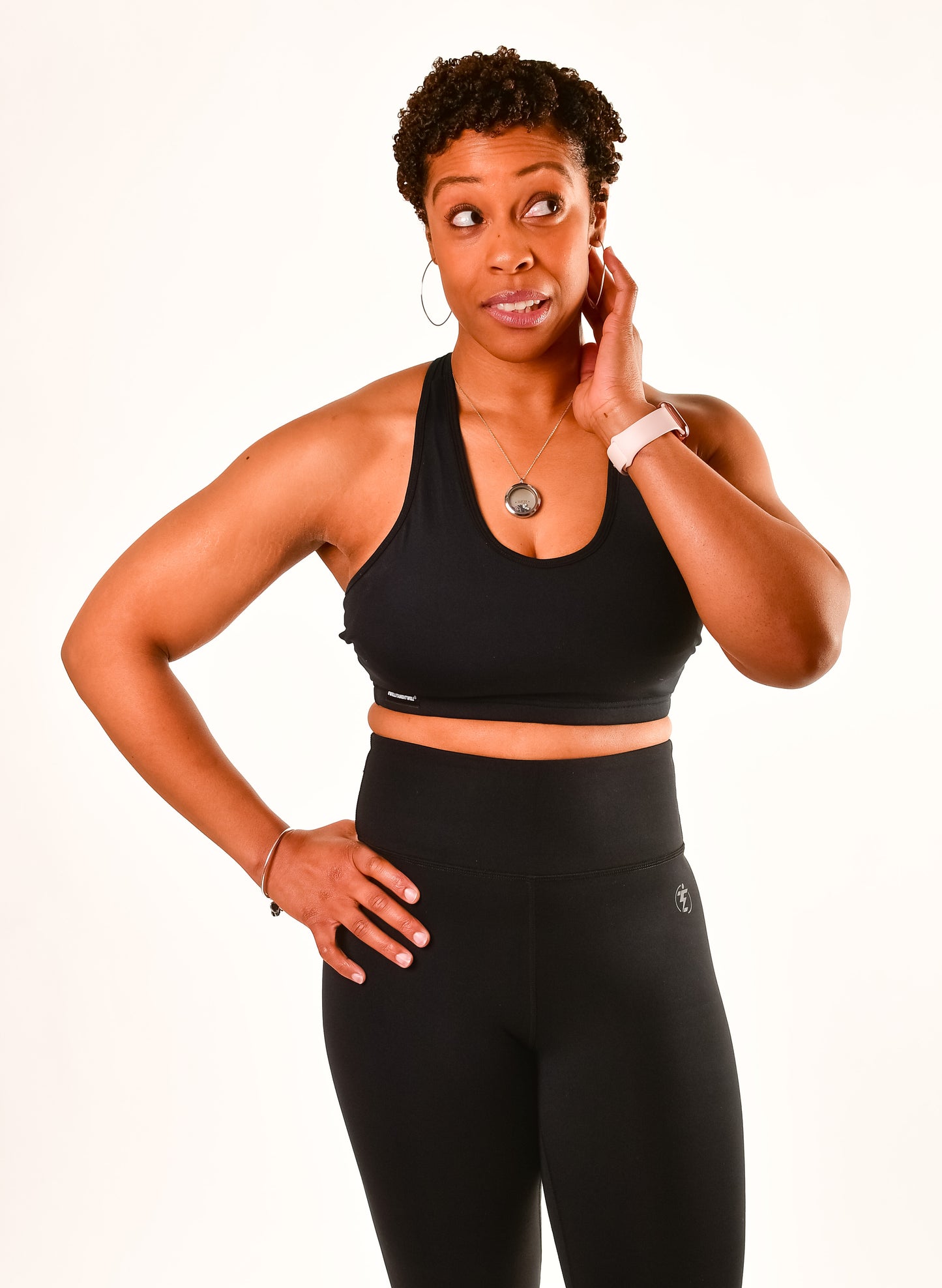 Woman in black sports bra and leggings with watch and necklace looking pensive.