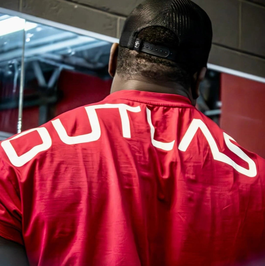 Back view of a person wearing a red 'Outlaws' branded jacket and a black baseball cap.