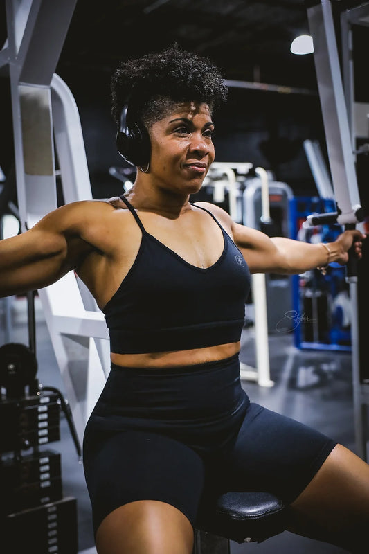 Woman in black sports bra and shorts working out on a chest press machine at the gym.