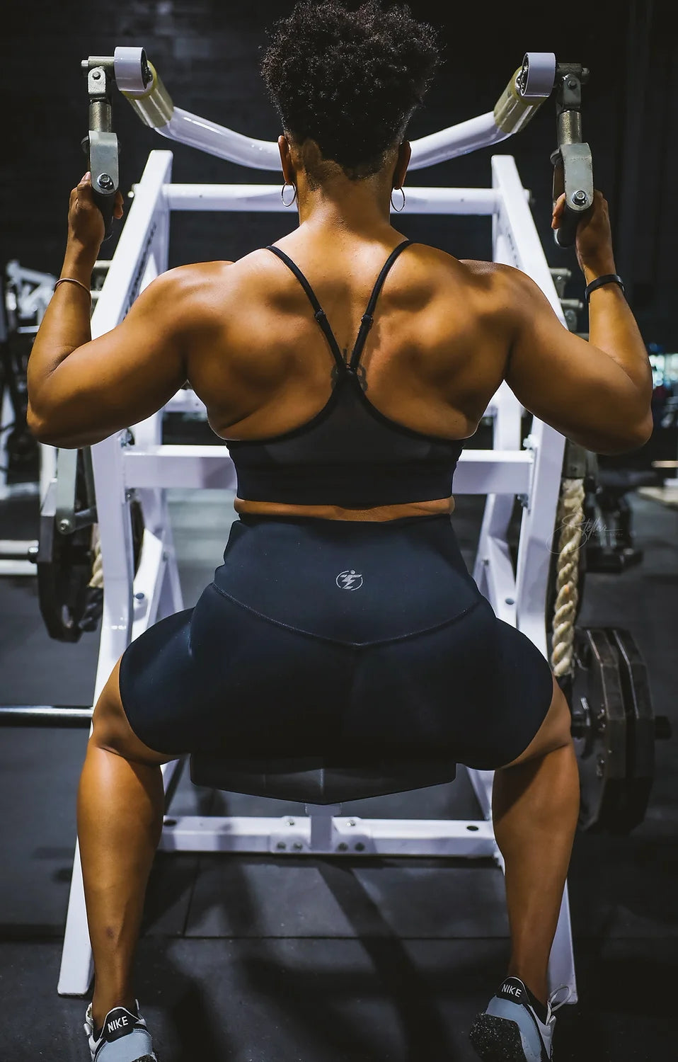 Woman working out on a lat pulldown machine wearing a black sports bra and black shorts.