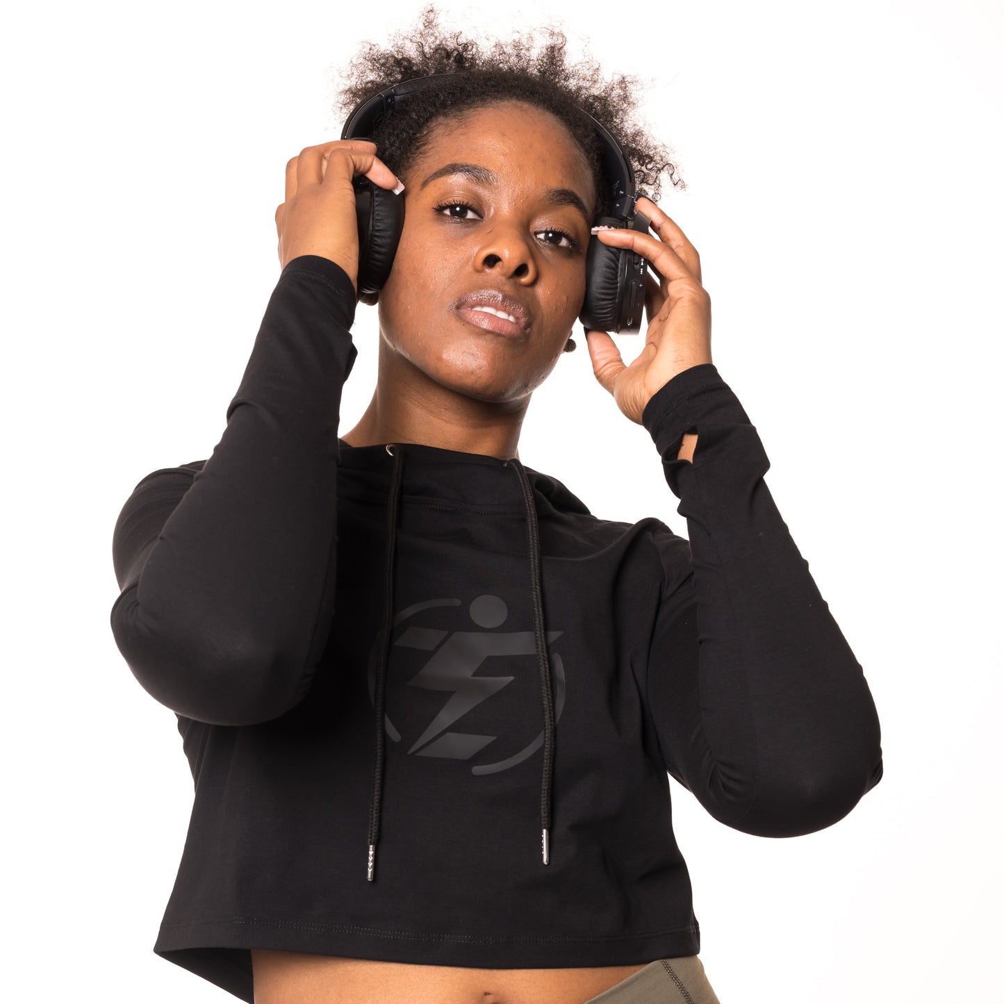Woman wearing black wireless headphones and a black cropped hoodie with a logo.