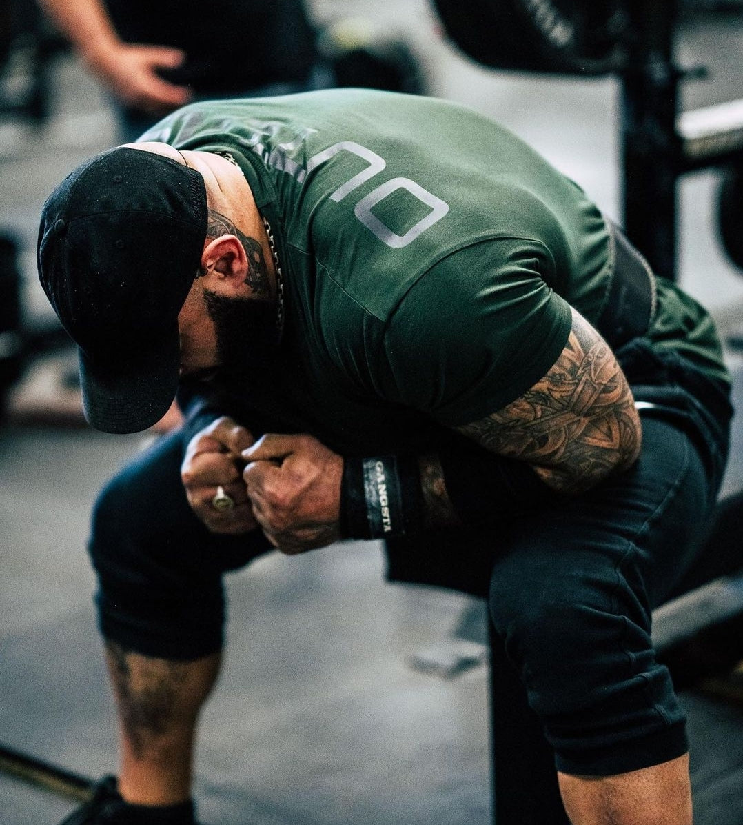 Man in olive green shirt and black pants wearing wrist wraps at the gym.