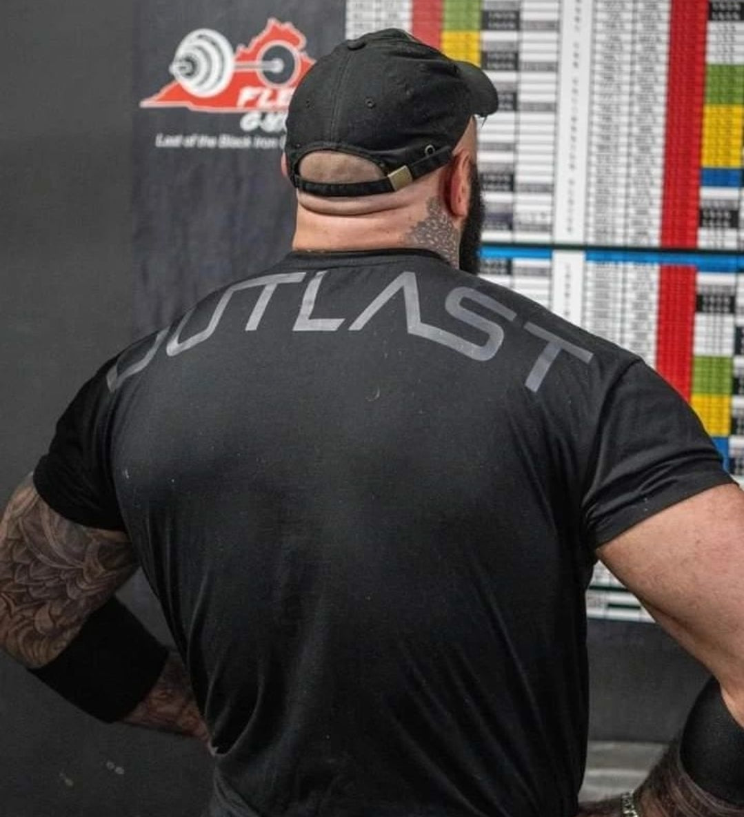 Man in black 'Outlast' t-shirt and cap at the gym, showcasing athletic apparel