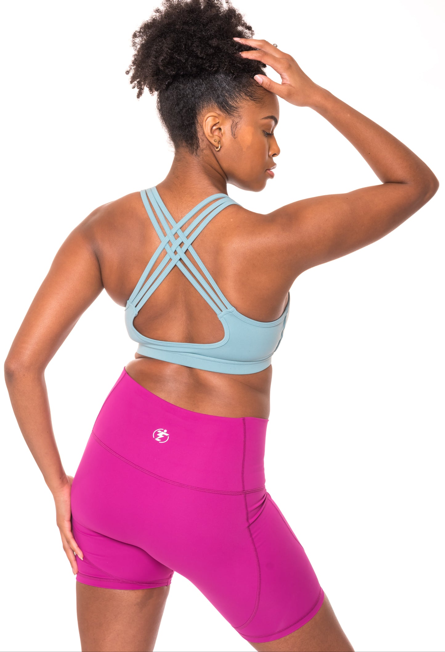 Woman wearing a blue sports bra with criss-cross straps and magenta running shorts.