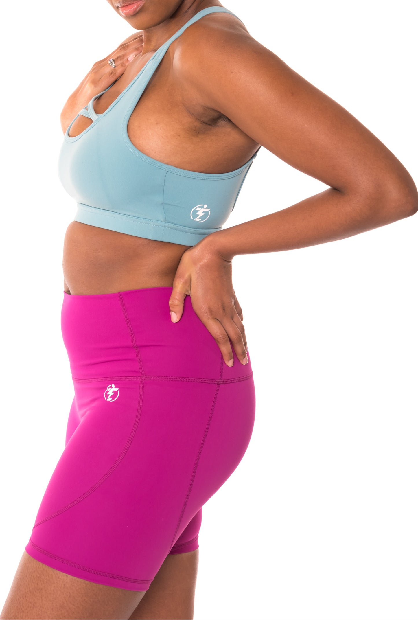 Woman in light blue sports bra and pink running shorts, side view. Fitness apparel.