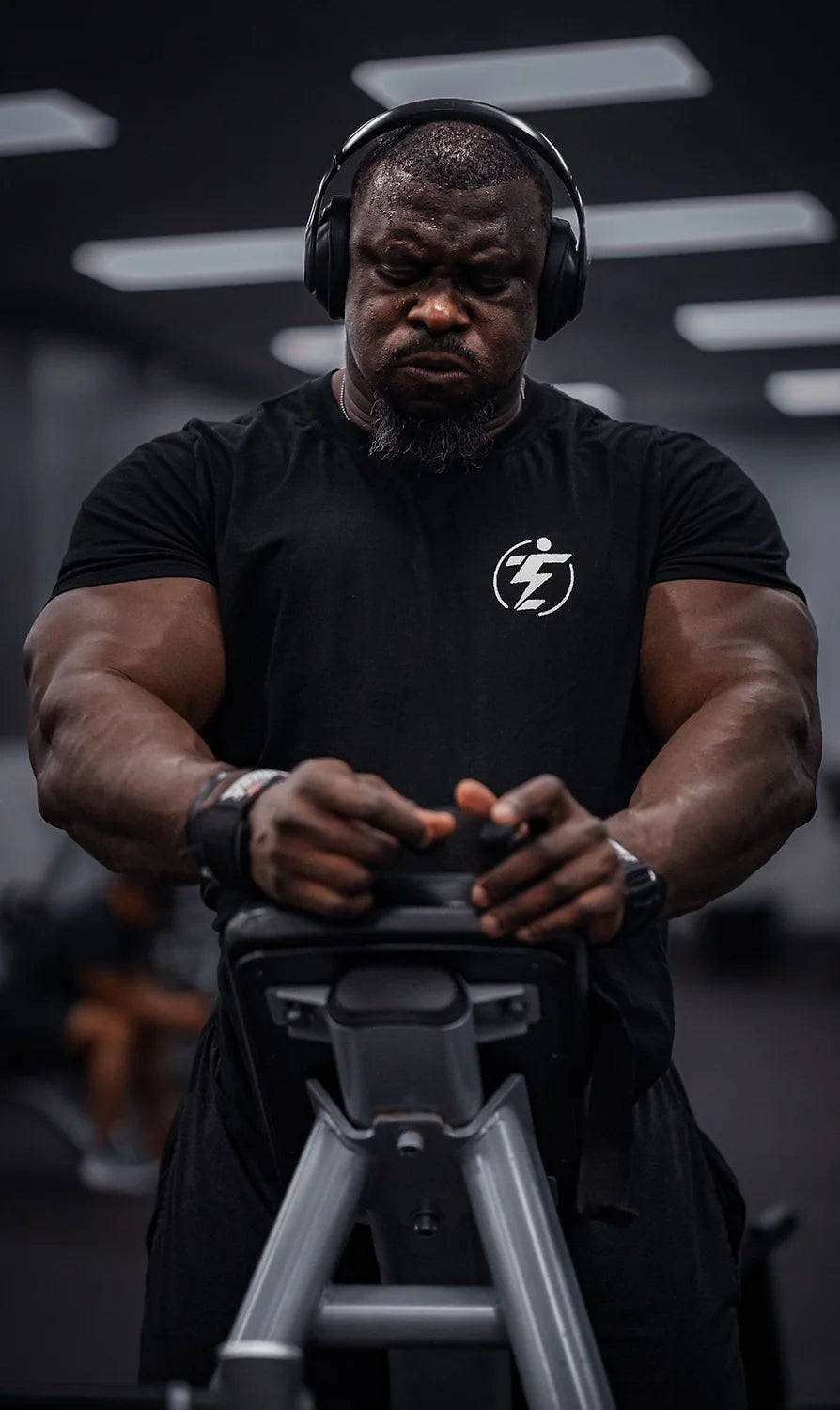 Man in black t-shirt and headphones using gym equipment. Weightlifting, exercise, fitness.