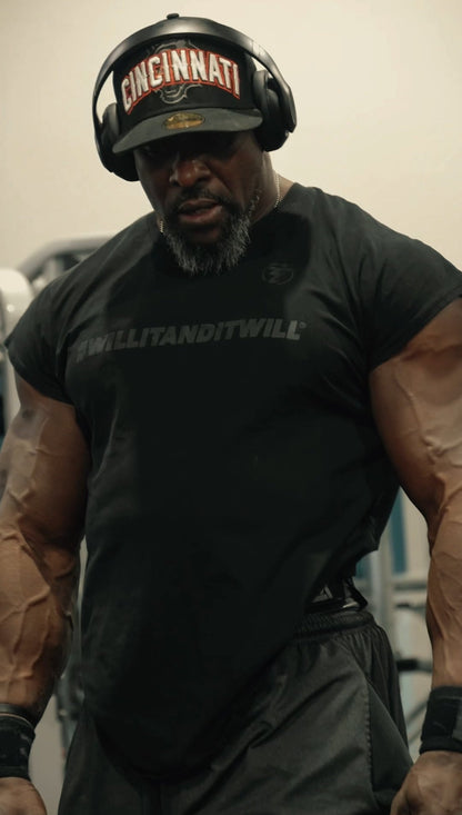 Person wearing a black t-shirt with text and a helmet with 'Cincinnati' on it, standing in a gym.