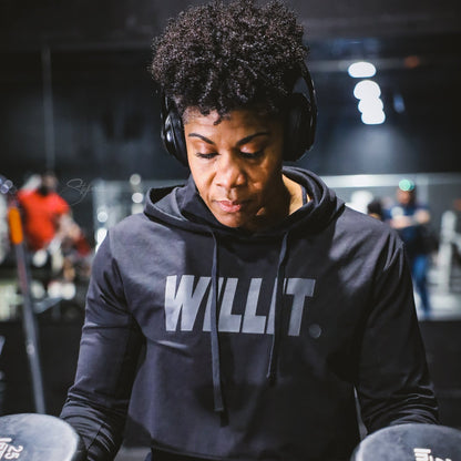 Woman in 'Willit' hoodie lifting weights at the gym, wearing headphones. Close up shot.